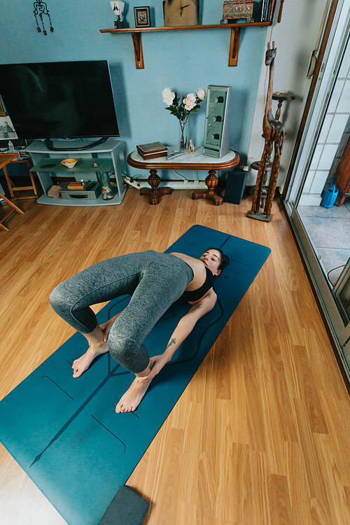 Young woman doing a yoga position over a professional yoga mat in a modern flat in the city