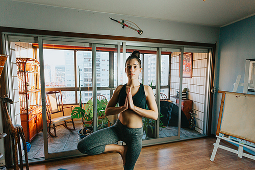 A young woman doing yoga at a modern flat in the city while smiling to camera with copy space