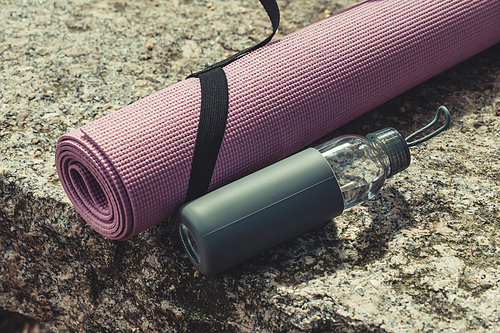 A yoga mat and a bottle of water resting over a rock with copy space