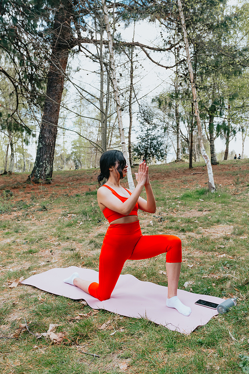 Young woman in fitness clothes doing yoga exercises over a yoga mat at the park during a sunny day