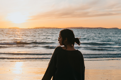 Woman in the beach looking a colorful sunset during a bright day with copy space
