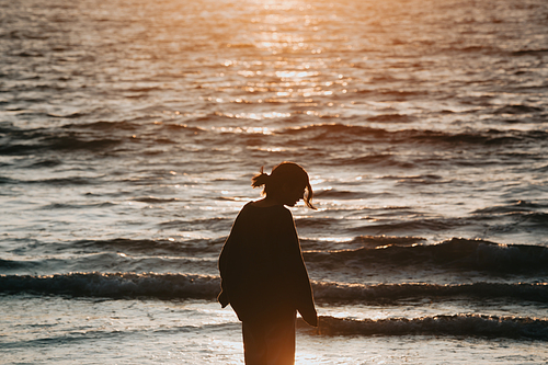 Young woman on spring clothes at the beach during a sunset