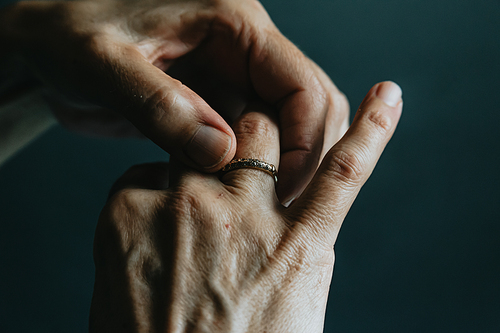 A pair of old hands grabbing a jewelry ring on the finger over a dark background