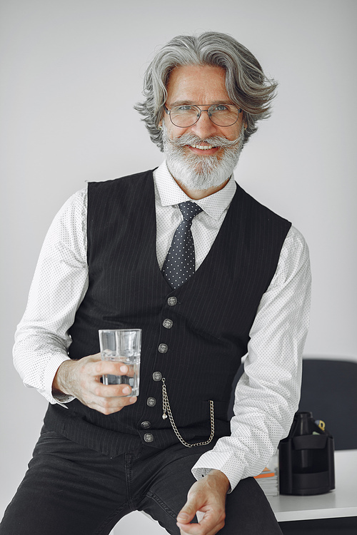 Close up portrait of grinning old-fashioned man. Elegant man in a studio. Grandfather with glass of water.