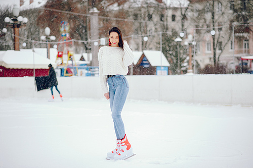 Girl in a winter city. Beautiful lady in a white sweater. Woman in a ice arena