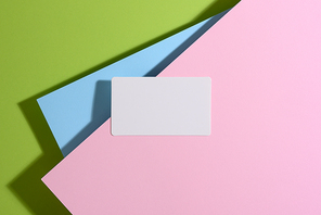 blank rectangular business card lies on a modern bright green background with blue and pink sheets of paper with a shadow. Business template, flat lay