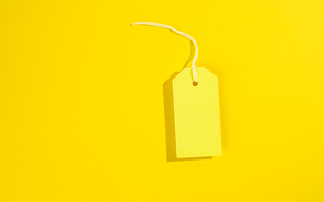 blank rectangular paper yellow price tag with white rope on yellow background, flat lay