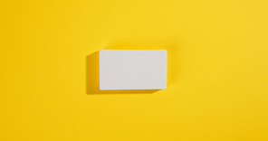 a stack of white rectangular business cards on a yellow background, company branding, address. View from above, flat lay
