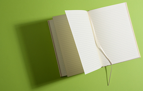 open notebook with blank white sheets on green background, top view