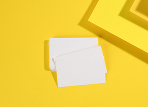 blank white rectangular business card on creative yellow background from sheets of paper with shadow, top view