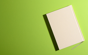 closed notepad on green background with shadow, top view, copy space