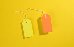 blank rectangular paper yellow and orange price tags with white rope on yellow background, top view