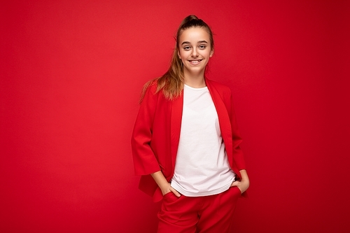 Photo shot of beautiful happy smiling brunette little girl wearing trendy red jacket and white t-shirt for mockup standing isolated over red background wall looking at camera. Free space