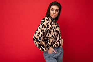Image of a beautiful young brunette woman dressed in animal printed blouse posing isolated over red background with copy space.