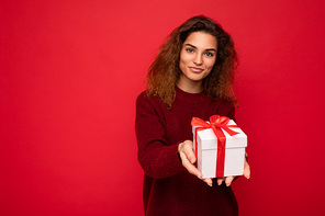 Shot of attractive positive smiling young brunette woman isolated over colourful background wall wearing everyday trendy outfit holding gift box and looking at camera. Copy space, mockup