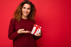 Shot of attractive positive smiling young brunette woman isolated over colourful background wall wearing everyday trendy outfit holding gift box and looking at camera. Free space
