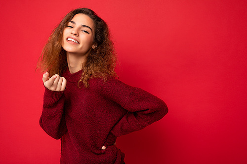 Portrait of young positive happy attractive brunette curly woman with sincere emotions wearing casual red sweater isolated on red background with copy space.