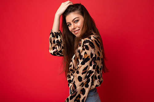 Photo of smiling young beautiful fashionable sexy brunette woman wearing stylish leopard blouse isolated on red background with empty space.