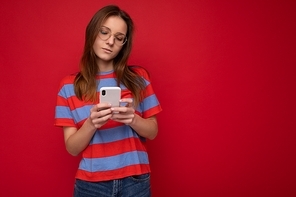 Beautiful young woman wearing casual clothes standing isolated over background surfing on the internet via phone looking at mobile screen.