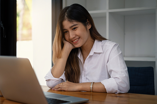 Cheerful young asian woman using laptop computer at home. Student female in living room. online learning, studying , online shopping, freelance, asean concept