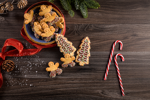 Christmas holiday background with gingerbread cookies, candy canes and evergreens over wooden table. Christmas and New year food. Christmas decoration and sweets on wood background.