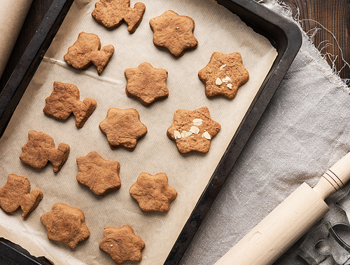 baked gingerbread cookies lie in a metal baking sheet on a brown table, top view