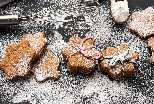 Star shaped baked gingerbread cookies sprinkled with powdered sugar on a black table, top view