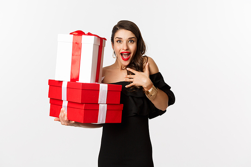 Celebration and christmas holidays concept. Excited and happy woman receive gifts, holding xmas presents and rejoicing, standing in black dress over white background.