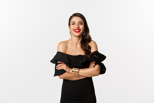 Beauty and fashion concept. Attractive female model in party dress and red lipstick, smiling pleased, looking happy, standing over white background.