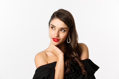 Fashion and beauty concept. Elegant woman with earrings and black dress, looking left sensual, standing over white background. Copy space