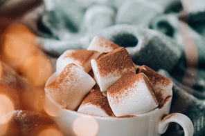 Cocoa drink with marshmallow and cacao powder on cozy winter sweater background. Christmas lights. Winter holiday home atmosphere. Holiday new year greeting card