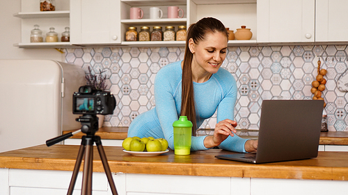 young woman in kitchen with laptop smiling. food Vlogger concept. a woman is recording a video about healthy eating. camera on a tripod.