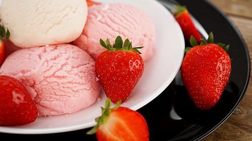 Delicious strawberry ice cream with fresh strawberrieson a white and black plate. Tasty summer cold dessert.