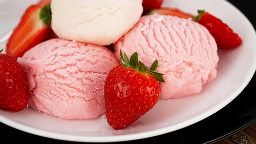 Delicious strawberry ice cream with fresh strawberrieson a white and black plate. Tasty summer cold dessert.