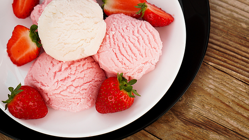 Delicious strawberry ice cream with fresh strawberrieson a white and black plate. Tasty summer cold dessert. Wood background