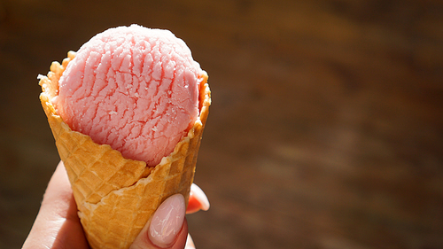 Close up image of woman hand holding fresh waffle cone with raspberry ice cream on the wooden background
