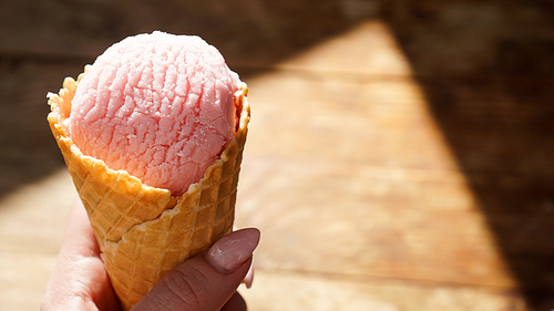 Close up image of woman hand holding fresh two waffle cones with raspberry ice cream on the wooden background