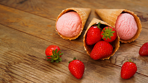 Strawberry ice cream in a waffle cone. Red berries and ice cream balls on a wooden background.