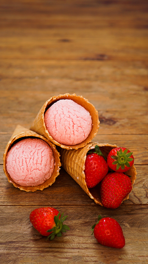 Strawberry ice cream in a waffle cone. Red berries and ice cream balls on a wooden background. Vertical photo