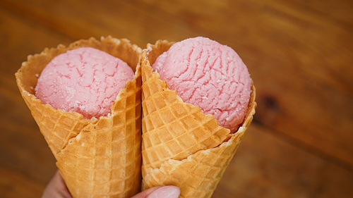 Close up image of woman hand holding fresh two waffle cones with raspberry ice cream on the wooden background
