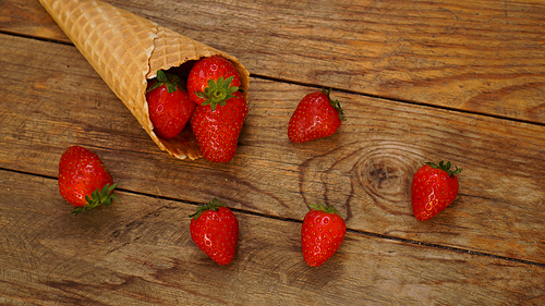 Ice cream cone with strawberries on a wooden background. Red berries in a waffle cone. Summer photo