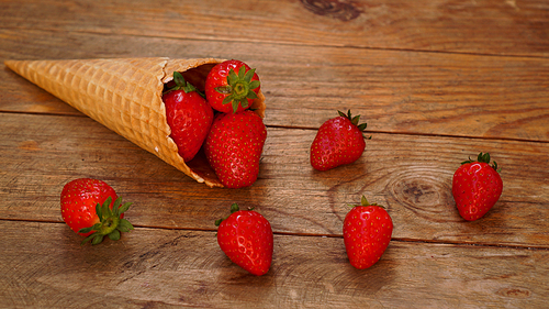 Ice cream cone with strawberries on a wooden background. Red berries in a waffle cone. Summer photo