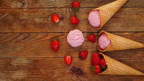Strawberry ice cream in a waffle cone. Red berries and ice cream balls on a wooden background. View from above