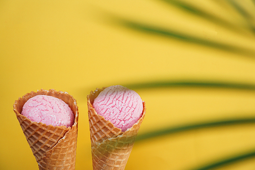 Two strawberry ice creams in a cone on a yellow background. Tropical leaf. Summer picture