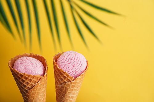 Two strawberry ice creams in a cone on a yellow background. Tropical leaf. Summer picture