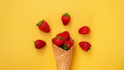 Ice cream cone with strawberries on a yellow background. Red berries in a waffle cone. Summer photo