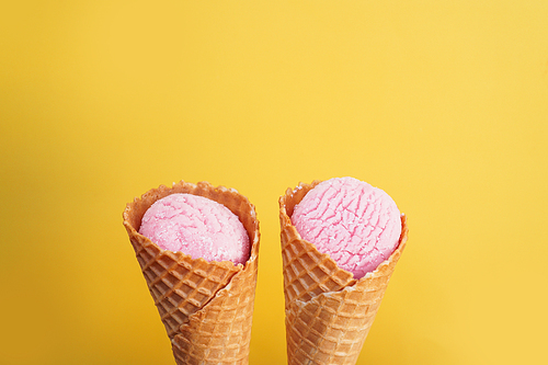 Delicious pink ice cream in a cone on a yellow background. Minimalism Concept.