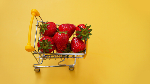 Fresh strawberries in a shopping cart on a bright yellow background. Fresh berries shopping concept.