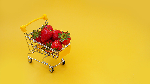 Fresh strawberries in a shopping cart on a bright yellow background. Fresh berries shopping concept.