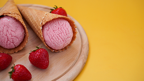 Strawberry ice cream in a waffle cone. Ice cream and berries on a yellow summer background